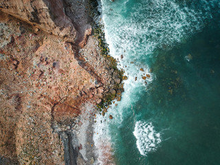 Aerial top view of sea waves hitting rocks on the beach with turquoise sea water. Amazing rock cliff seascape in the Portuguese coastline.