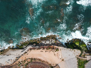 Aerial top view of sea waves hitting rocks on the beach with turquoise sea water. Amazing rock cliff seascape in the Portuguese coastline.