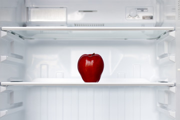A lone red apple on a shelf in an empty fridge. One fresh apple in an empty clean refrigerator. Fruits is cooling in storage.