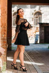 the girl is posing smiles. Emotional portrait of Fashion stylish portrait of pretty young woman. city portrait. brunette in a black dress. expectation. dreams