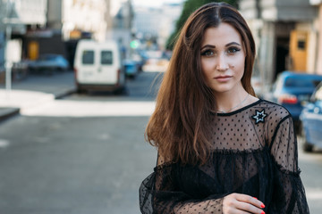 Fototapeta premium Emotional portrait of Fashion stylish portrait of pretty young woman. city portrait. sad girl. brunette in a black dress. expectation. dreams. girl - night in the middle of the day