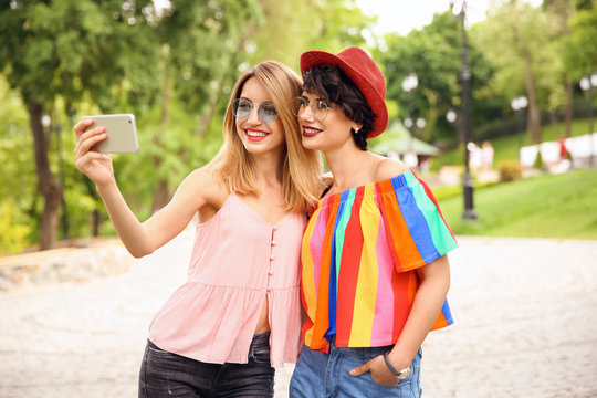 Young women in stylish clothes taking selfie outdoors