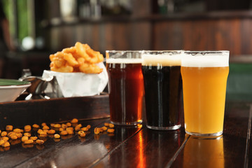 Glasses of tasty beer and snacks on wooden table in bar