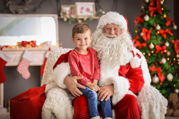 Obraz premium Little boy sitting on authentic Santa Claus' lap indoors