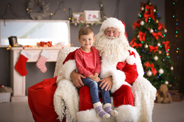 Fototapeta na wymiar Little boy sitting on authentic Santa Claus' lap indoors