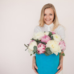 Stylish flower delivery, gift. Woman with flowers in a hat box. Bouquet of peonies.