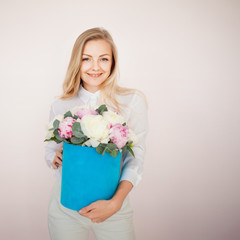 Stylish flower delivery, gift. Woman with flowers in a hat box. Bouquet of peonies.