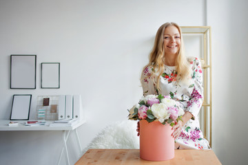 Fototapeta na wymiar Happy blonde woman in a modern office with flowers in a hat box. Bouquet of peonies.