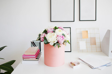 Flower delivery to office. Working space, table with notebooks and magazines. Luxurious bouquet of peonies in pink box.