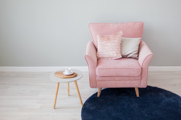 Stylish pink velvet chair with pillows. Stands against a light gray wall.