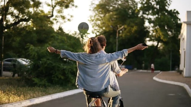 Happy, smiling couple riding electro bike in the park. Girl with outstretched hands. Enjoyment, hanging outdoors in the park, dating