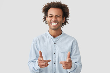 Positive mixed race male startup owner rejoices success, points at camera, has broad smile, being...