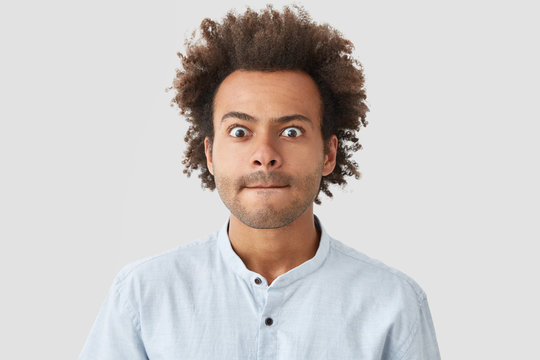 Headshot of attractive stunned mixed race male employee with pressed lips, feels embarrassed and suprirsed, being invited to meeting with business competitor, isolated over white background.