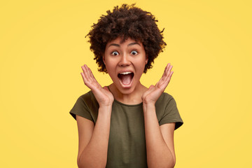 Surprised happy young dark skinned female stands in big shopping mall, glad to see big discounts on...