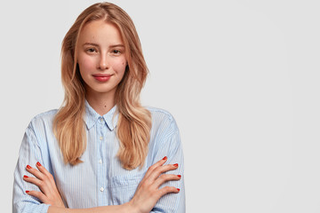 Pleased lovely young European female has cheerful expression, keeps arms folded, dressed in...