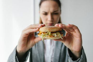 A young girl shows that she does not like a burger. Conceptual image of refusal from unhealthy eating.