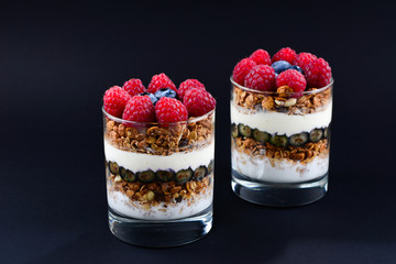 Healthy blueberry and raspberry parfait in a glass on a black background. Two portions. Space for text or design.
