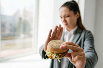 A young girl shows that she does not like a burger. Conceptual image of refusal from unhealthy...