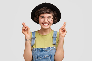Cute cheerful young Caucasian female has feeling of hope, crosses fingers for good luck, has...