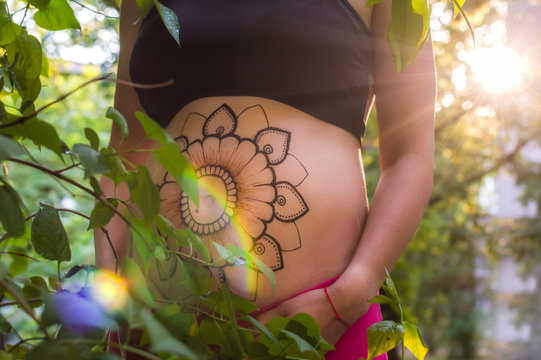 only the belly of a pregnant woman with a mehendi on her stomach close-up in the rays of the sun