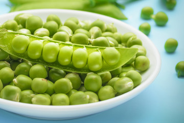 Beautiful half of a fresh pea pod with peas in a pile of peas in a white plate