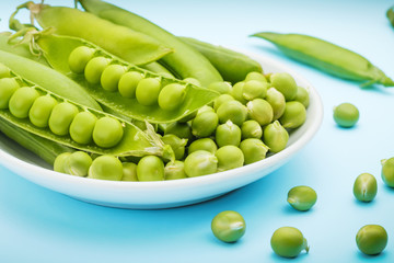 A white plate filled with pods and peas of green peas. In the focus is an open pea pod.
