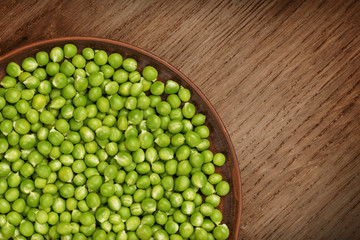 Fresh green peas in a brown plate. Top view