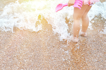 Baby legs in the sea foam with toy on the beach with sunlight, summer concept