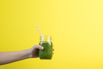 Woman hand holding smoothie shake against colored wall. Drinking green healthy smoothie concept.