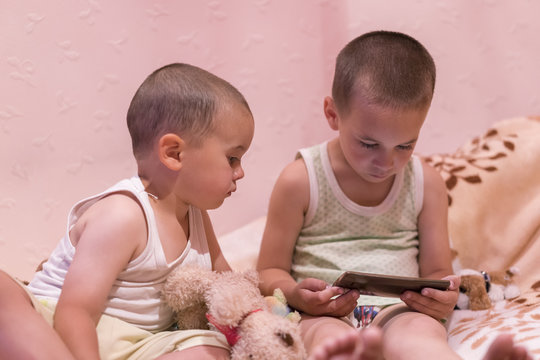 children in the bedroom watching cartoons. children play on smarfone. two brothers in the bedroom look at the smartphone.
