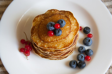 Homemade pancekes with fresh blueberries and red currants on white plate