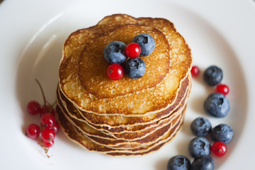 Homemade pancekes with fresh blueberries and red currants on white plate