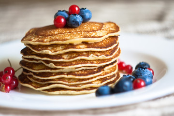 Homemade pancekes with fresh blueberries and red currants on white plate