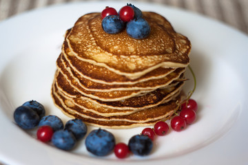 Homemade pancekes with fresh blueberries and red currants on white plate