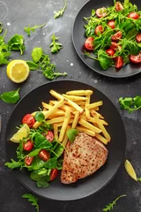 Poster Fried Tuna Steaks on Black Plate with Fresh Green, Tomato Salad, lemon and french fries. healthy sea food © grinchh