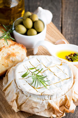 Baked camembert cheese. Fresh Brie cheese and a slice on a wooden board with nuts, honey, rosemary, baguette bread grilled toasts and leaves. Brie type of cheese. Italian, French cheese.