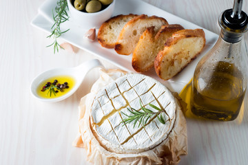 Baked camembert cheese. Fresh Brie cheese and a slice on a wooden board with nuts, honey, rosemary, baguette bread grilled toasts and leaves. Brie type of cheese. Italian, French cheese.