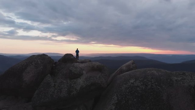 Aerial view of the lonely man standing on top of a cliff and enjoying the sunset.