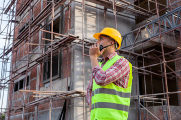 Naklejka na ściany i meble Architect engineer using walkie-talkie talking with assistant while working front of building site.