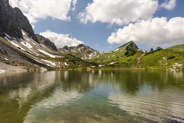 Crystal clear water of alpine lake Lache in Tannheimer high valley with mountain refuge Landsberger Hut in the background, Tyrol, Austria
