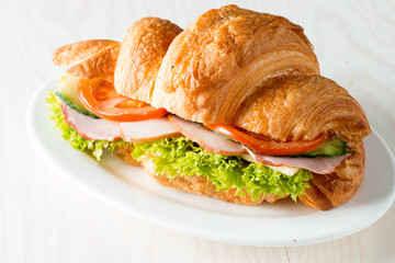Fresh croissant or sandwich with salad, ham, jamon, prosciutto, salami, cheese, chicken, tomatoes on wooden background. Morning breakfast concept. Healthy and fast food.