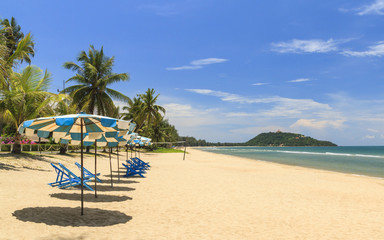 Fototapeta na wymiar Beach Chairs With Umbrellas On The White Sand Beach With Cloudy Blue Sky.