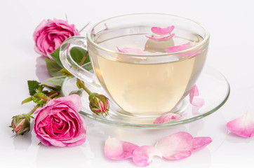Obraz na płótnie Canvas Glass cup of Tea with roses and petals