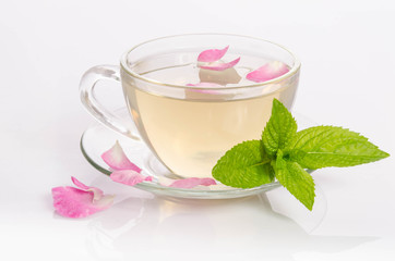 Glass cup of Tea with mint leaves and rose petals on light table