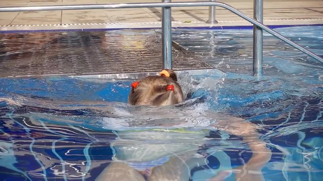 cute little girl is plunging inside water of swimming pool, closing eyes and holding breath