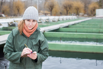 Female worker of fish farm writing something in notebook