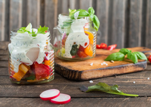 Fresh vegetable salad in jars with homemade dressing on wooden table.