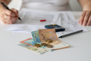 Verschiedene Euro Geldscheine und Münzen auf einem Schreibtisch in einem Büro hinter dem eine...