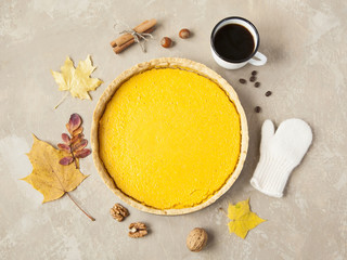 Pumpkin cake with autumn leaves, nuts, cinnamon, mitten and mug of coffee.