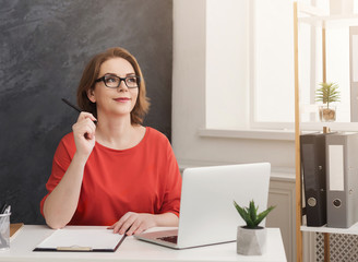 Business woman using laptop and writing notes in office